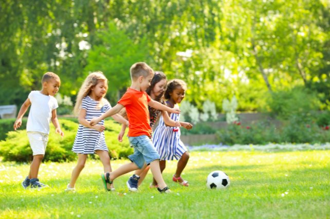 Un grupo de chicos juega a la pelota en el pasto de una plaza