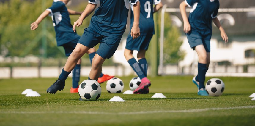 Chicos con camisetas de equipo entrenando con pelotas y conos en una cancha de fútbol