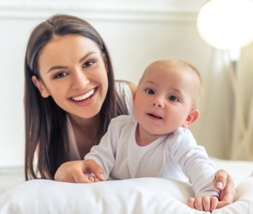 Una mamá sonriente junto a su bebé, acostados sobre una almohada