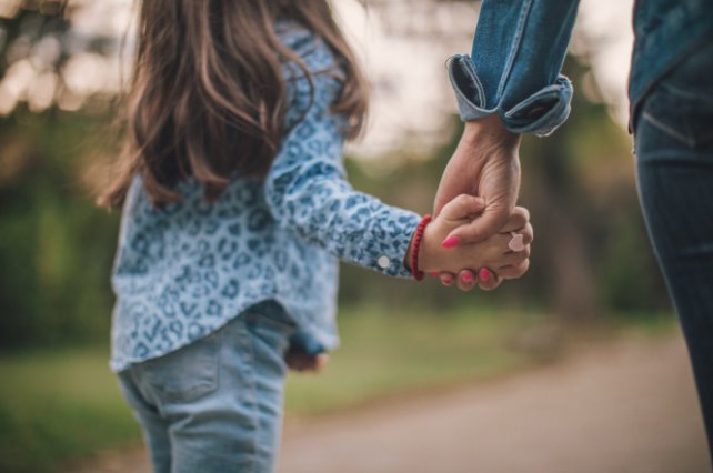 Una nena camina de la mano de su mamá por un sendero