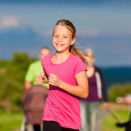 Una nena con remera rosa sale a correr sonriendo junto a su familia